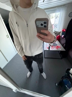 Vit zip hoodie med huva - Säljer en stilren vit hoodie med dragkedja och huva. Hoodien har fickor framtill och ribbade muddar vid ärmar och nederkant. Perfekt för en clean och enkel look. Materialet känns mjukt och bekvämt, och modellen är klassisk med normal passform.