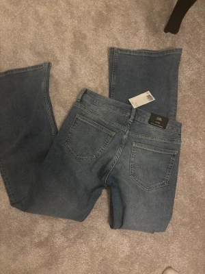 Blå bootcut jeans från H&M - Säljer ett par blå bootcut jeans från H&M med klassisk femficksmodell och normal midja. Jeansen har en snygg tvättad look och är tillverkade i mjuk denim. Perfekta för dig som gillar en avslappnad men trendig stil.
