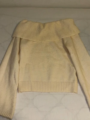 Off shoulder stickad tröja cremevit - Trendig off shoulder stickad tröja i cremevitt med bred ribbad krage och långa ärmar. Perfekt för dig som vill ha en mysig men ändå stylish look. Tröjan har ribbade muddar vid ärmslut och nederkant. Materialet känns mjukt och bekvämt.