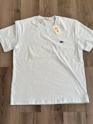 🩵Ljusblå Lacoste t-shirt i bomull🩵 - Snygg ljusblå t-shirt från Lacoste med klassisk krokodillogga på bröstet. T-shirten är i mjuk bomull och har en enkel, stilren design med rund hals och korta ärmar. Perfekt för en clean och fräsch look. Storleken är L men passar S.