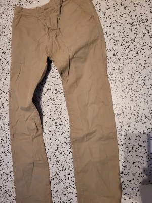 Beiga chinos med raka ben - Snygga beiga chinos med raka ben och klassisk passform. Byxorna har dragkedjegylf och knappar i midjan samt sidofickor. Tillverkade i ett mjukt bomullstyg som känns skönt mot huden. Perfekta för en clean och avslappnad stil. Stl 30/32