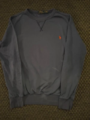 Mörkblå sweatshirt från Polo Ralph Lauren - Mörkblå sweatshirt från Polo Ralph Lauren med klassisk rund halsringning och ribbade muddar. Tröjan har den ikoniska röda logotypen broderad på bröstet och är tillverkad i mjuk bomullsblandning. Perfekt för en avslappnad och stilren look. Litet hål på baksidan av armen som inte syns med tröjan på, bild 5. 