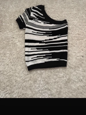 Svartvit oneshoulder stickad topp - Säljer en unik stickad topp i svart och vitt med grafiskt randigt mönster. Köpt på vinted men aldrig använd av mig