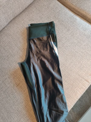 Mörkgröna Björn Borg leggings - Snygga sportleggings i mörkgrönt med vit detalj vid höfterna. Hög midja och åtsittande passform, perfekta för träning eller gym. Tillverkade i stretchigt och glansigt material som ger bra rörelsefrihet. Märket Björn Borg har slitage, se bilder.  Jag tycker att de sitter riktigt bra på. Har inte glidit ner för min del.