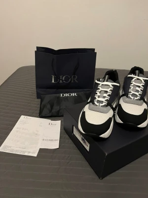 Dior B22 sneakers svart/vit - Snygga Dior B22 sneakers i svart, vitt och grått med chunky sula och coola detaljer. Ovandelen är i mesh och skinn med snörning och rund tå. Perfekta för dig som vill ha en exklusiv och trendig look.
