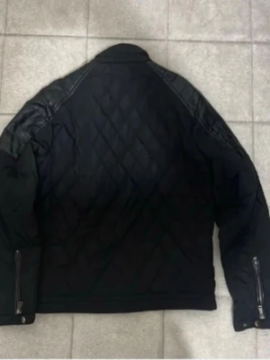 Svart pufferjacka från Zara Man - Snygg svart pufferjacka från Zara Man med quiltat mönster och dragkedjor vid ärmsluten. Jackan har en modern passform och är tillverkad i ett slitstarkt material som håller värmen under kalla dagar. Perfekt för dig som vill ha en stilren vinterjacka.