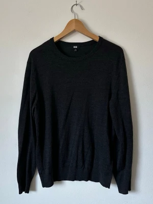 Mörkgrå stickad tröja från Uniqlo - En stilren mörkgrå stickad tröja från Uniqlo med rund halsringning och långa ärmar. Tröjan är tunn och mjuk, perfekt för lager på lager och enkel att matcha till olika outfits. Materialet ser ut att vara en blandning med merinoull. 8D14 