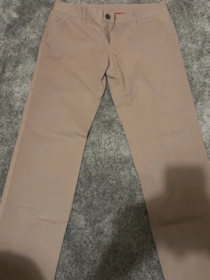 Beige chinos med rak passform - Snygga beige chinos med rak passform och klassisk design. Byxorna har bälteshällor, knappgylf och två sidofickor. Perfekta för en clean och stilren look. Materialet känns mjukt och bekvämt, troligtvis bomull eller bomullsblandning.