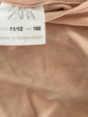 Beige topp med puffärm från Zara - Söt beige topp från Zara med puffiga kortärmar och spetsdetaljer. Tillverkad i mjuk bomull och har en avslappnad passform. Perfekt för dig som gillar en enkel men ändå trendig stil.