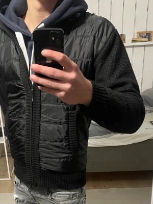 Svart stickad cardigan  - Säljer en svart cardigan med stickade ärmar och ribbade muddar. Cardiganen har dragkedja framtill och två fickor. Storlek M men passar som S.