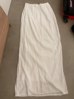 Vit långkjol i strukturerad bomull - Lång, vit kjol i ett strukturerat bomullstyg. Kjolen har en rak och enkel passform som ger en clean och stilren look. Perfekt för dig som gillar minimalistisk stil och vill ha något luftigt till sommaren.