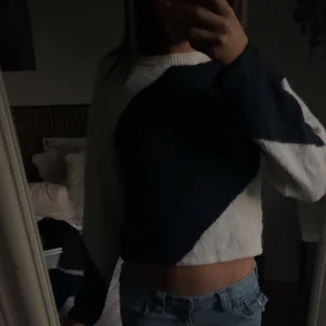 Stickad tröja med blå och vit färgblock - Säljer en stickad tröja med cool färgblock-design i mörkblått och vitt. Tröjan har croppad passform och långa ärmar. Perfekt till jeans för en avslappnad look.
