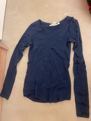 Mörkblå långärmad topp - En enkel och stilren mörkblå långärmad topp med rund halsringning. Tillverkad i ett mjukt och stretchigt material som sitter skönt på kroppen. Perfekt att matcha med jeans eller kjol för en clean look.