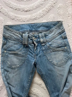Pepe jeans Ljusblå jeans med bred linning - Unika ljusblå jeans med bred linning och dubbla bälteshällor. Jeansen har stora, rundade framfickor och en avslappnad passform. Tillverkade i klassiskt denimtyg som ger en cool och avslappnad vibe.