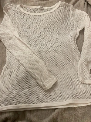 Vit mesh långärmad topp - Säljer en vit mesh topp med lång ärm och rund hals. Toppen är helt genomskinlig med nätstruktur och har en avslappnad passform. Perfekt att styla lager på lager för en trendig look.