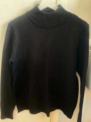 Svart polotröja från VILA - Klassisk svart stickad polotröja från VILA med hög krage och långa ärmar. Tröjan har en enkel och stilren design, perfekt för lager på lager. Materialet är mjukt och bekvämt, vilket gör den skön att bära under kyliga dagar.