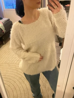 Krämvit fluffig stickad tröja - Mysig krämvit stickad tröja med fluffig textur och rund halsringning. Tröjan har långa ärmar och en avslappnad passform, perfekt för lager-på-lager. Passar dig som gillar en enkel men trendig look.