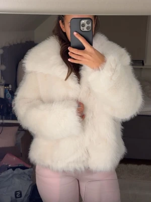 Vit fluffig fuskpälsjacka - Säljer en supermjuk och fluffig vit fuskpälsjacka med bred krage och rak passform. Jackan har en lyxig look och stängs framtill. Perfekt för dig som vill ha en statement piece till vintern. Passar till allt från jeans till klänning.