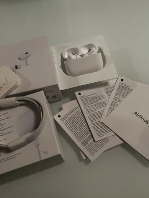 Apple AirPods Pro med laddningsetui - Säljer ett par vita Apple AirPods Pro med trådlöst laddningsetui. Inkluderar originalförpackning, USB-C laddkabel och manualer. Snygg och kompakt design i plast med silikontoppar för bra passform. Perfekt för dig som vill ha grymt ljud och smidig anslutning till iPhone.