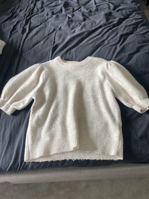 Vit stickad tröja med puffärm - Mysig vit/ beige stickad tröja med puffärmar och ribbade muddar. Tröjan har rund halsringning och är gjord i ett mjukt, fluffigt material som känns skönt mot huden. Perfekt för dig som gillar en enkel men trendig look.
