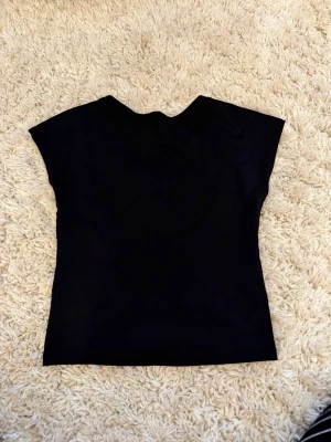Öppen rygg  - Säljer en svart croppad topp med korta ärmar och öppen rygg. Toppen har en enkel och stilren design som passar perfekt till jeans eller kjol. Materialet känns mjukt och stretchigt, vilket gör den bekväm att bära.