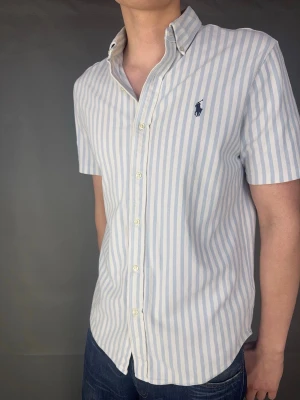 Kortärmad Ralph Lauren skjorta - Kortärmad Ralph Lauren skjorta Märke: Ralph Lauren Storlek: L Passform: Färg: Randig vit/blå Skick: Mycket bra Beskrivning: utan defekter. Modellen på bilden: 183 cm / 75 kg