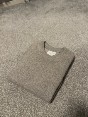 Stickat vailent tröja - Säljer en stilren beige stickad tröja från Vailent i mjuk merinoull. Tröjan har rund halsringning och ribbade muddar vid halsen. Perfekt för dig som gillar minimalistisk och klassisk stil.