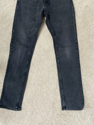 Svarta Nudie jeans Co - Snygga svarta jeans med rak passform och diskret tvättad look. Klassisk femficksmodell och bälteshällor. Jeansen är tillverkade i denim och har en stilren vibe som passar till det mesta.