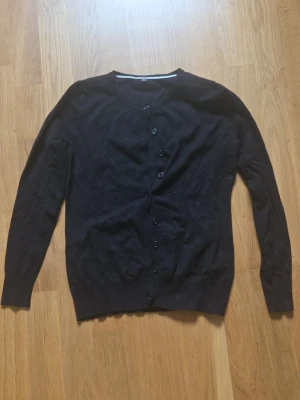 Svart basic kofta med knappar - En enkel svart kofta med rund halsringning och knäppning framtill. Långärmad modell i mjukt, tunt material som passar perfekt till lager på lager. Klassisk och stilren design utan synliga loggor eller detaljer.