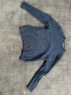 Mörkblå kabelstickad Ralph lauren tröja - Mörkblå kabelstickad tröja med rund hals och ribbade muddar vid ärmslut och nederkant. Tröjan har ett klassiskt mönster och är perfekt för lager på lager. Passar dig som gillar en enkel men stilren look.