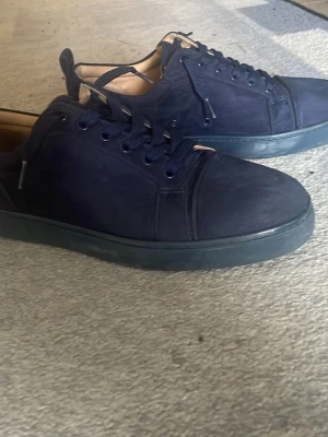 Louboutins - Snygga mörkblå sneakers med låg profil och klassisk snörning. Skorna har en stilren design med ovandel i mockaliknande material och matchande mörkblå sula. Perfekta för dig som gillar en clean och enkel look.