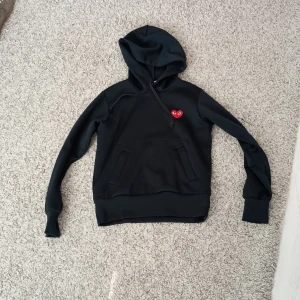 Svart hoodie Comme des Garçons Play - Svart hoodie från Comme des Garçons Play med klassiskt rött hjärta med ögon broderat på bröstet. Tröjan har huva med snörning, magficka och långa ärmar. Mjuk och skön bomullskänsla, perfekt för chill dagar. Passar mer som xs. Hör av er vid frågor 🤝