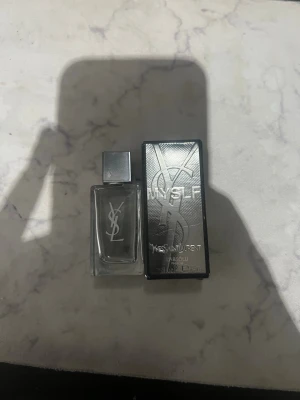 YSL MYSLF Absolu Eau de Parfum - En elegant parfym från Yves Saint Laurent, MYSLF Absolu, i en genomskinlig glasflaska med silverfärgat lock och tydlig YSL-logga. Medföljer gör en stilren silverfärgad kartong med präglad logga. Perfekt för dig som gillar exklusiva dofter.