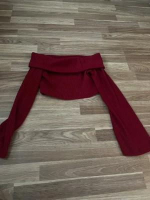 Röd off shoulder stickad tröja - Trendig röd stickad tröja med off shoulder-design och långa vida ärmar. Ribbstickat material som ger en snygg och bekväm passform. Perfekt för dig som vill sticka ut med en cool och modern look.