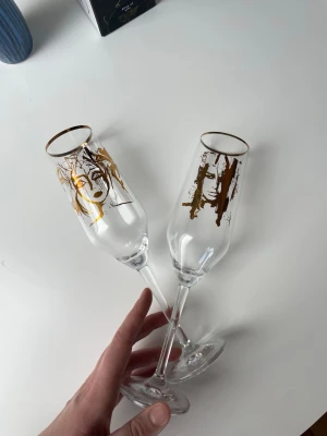 Champagneglas Carolina Gynning - Två oanvända champagneglas från Carolina Gynning med unika konstmotiv i guld. Motiven heter 'Slice of Life' och 'Wild Woman' och levereras i originalförpackning. 200 kr styck eller 300 kr för båda. 