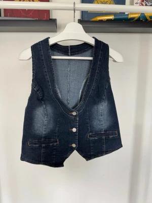 Mörkblå jeansväst med knappar - Snygg mörkblå jeansväst med djup V-ringning och tre silverfärgade knappar framtill. Matchande barrel-jeans finns på min profil om det är något som låter intressant! 