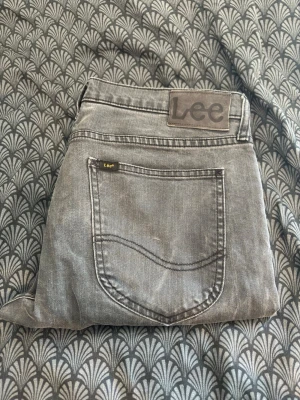 Grå jeans från Lee - Snygga grå jeans från Lee med klassisk femficksdesign och raka ben. Jeansen har Lee-logga på bakfickan och bakre linningen. Tillverkade i denim med tydliga sömmar och en tvättad look. Pruttmåt fungerar vid snabb affär!