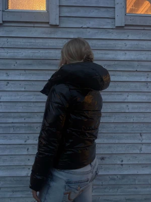Svart pufferjacka från Calvin Klein - Säljer en svart, glansig pufferjacka från Calvin Klein Jeans. Jackan har en hög krage och vadderad design som håller dig varm under kalla dagar. Märkesloggan syns diskret på ärmen och även vid bröstet. Perfekt för dig som vill ha en stilren och trendig vinterjacka. Pris går att diskutera!!