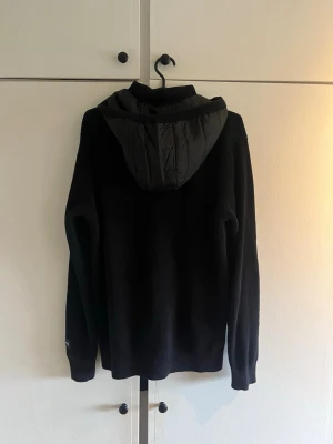 Svart cardigan med dragkedja och huva - Svart cardigan med hel dragkedja framtill och avtagbar nylonhuva i Massimo Dutti stuk! Helt slutsåld, säljer till bra pris eftersom den sitter lite tajt på mig. Jag är 190cm 76kg. Hör av er vid fler frågor eller funderingar!