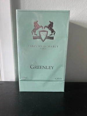 Parfums de Marly Greenley 125ml - Greenley från Parfums de Marly är en exklusiv parfym i en mintgrön kartong med silverdetaljer och logotyp med två hästar. Förpackningen är elegant och modern, och innehåller 125 ml Eau de Parfum. Perfekt för dig som gillar lyxiga dofter.