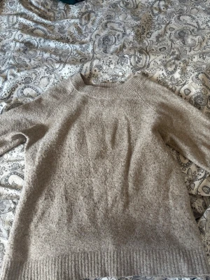Beige stickad tröja i ullmix - Mysig beige stickad tröja med rund hals och ribbade muddar vid ärmslut och nederkant. Tröjan har en avslappnad passform och är tillverkad i en mjuk ullmix som håller dig varm under kyliga dagar. Perfekt att matcha med jeans eller kjol.