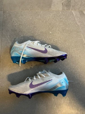 Mercurial vapor 16 elite FG chromatic storlek 43 - Säljer ett par Nike Mercurial fotbollsskor i vitt med lila swoosh och detaljer. Skorna är skit snygga enligt mig men kan ej ha dem pågrund av storlek. Dem är använda endast en träning, ungefär 3000kr nypris 
