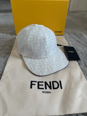 Vit keps med FF-mönster från Fendi - Snygg vit keps från Fendi med det klassiska FF-logomönstret över hela kepsen. Kepsen har böjd skärm och justerbar rem bak. Tillverkad i ett slitstarkt tygmaterial levereras INTE med originalpåse och tagg