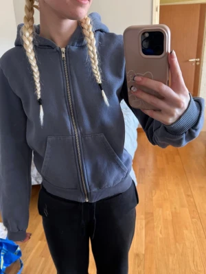 Blå zip-hoodie med huva - Säljer en blå hoodie med dragkedja och huva. Tröjan har ribbade muddar vid ärmslut och nederkant samt en stor magficka framtill. Perfekt för en avslappnad och stilren look. Materialet är mjukt och bekvämt, troligtvis bomullsblandning.