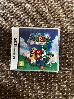 Super Mario 64 DS till Nintendo DS - Super Mario 64 DS är ett klassiskt plattformsspel till Nintendo DS med färgglad omslagsdesign. Spelet har Mario, Luigi, Wario och Yoshi på framsidan och är i en vit plastbox. Perfekt för dig som gillar retrospel och äventyr.