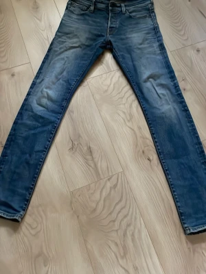 Blå slim fit jeans med slitningar - Snygga blå slim fit jeans med lätt slitna detaljer och tvättad look. Klassisk femficksmodell med knappar och knapp i midjan. Jeansen har smala ben och är tillverkade i denim, perfekt för en trendig vardagsstil.