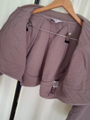 Ljuslila jacka från Adidas Stella McCartney - Snygg ljuslila jacka från Adidas Stella McCartney-kollektionen. Mycket lämpling för sommar säsongen. Det är en crop top-model. Jackan har en croppad passform, dragkedja och är tillverkad i ett mjukt, quiltat material med dekorativa sömmar. 