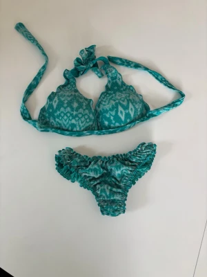 Turkos calzedonia bikini  - Snygg turkos bikini med unikt mönster och snörning i halsen. Bikinin har volangdetaljer på både överdel och underdel, och är perfekt för strandhäng. Materialet känns mjukt och stretchigt, vilket ger en bekväm passform. Bikiniöverdel 85B