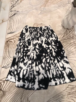 Svartvit mönstrad kjol från H&M - Säljer en svartvit kjol från H&M med coolt abstrakt mönster. Kjolen har resår i midjan och är lätt utställd med plisserad struktur. Perfekt för dig som gillar en unik och trendig stil. Är öppen med prisförslag😊