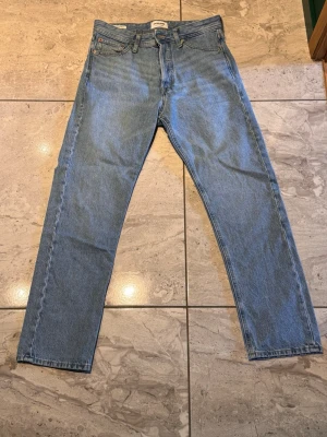 Blåa jack&jones jeans  - Klassiska jack&jones jeans i ljusblå denim. Jeansen har knappgylf och den ikoniska läderpatchen bak i midjan. Perfekta för en avslappnad och tidlös stil.